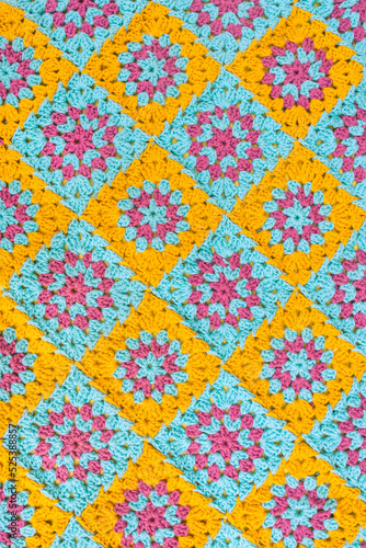 Top view of crochet afghan, made of colorful granny square motifs of yellow, turquoise and lilac colors.