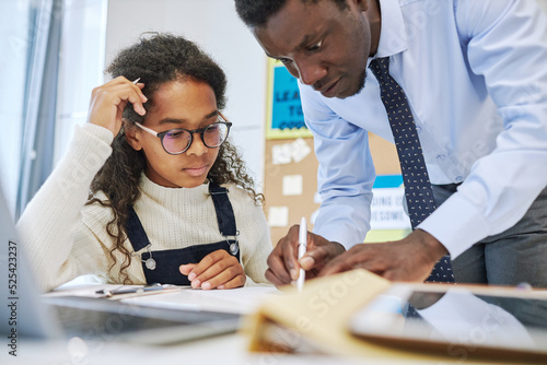 Portrait of male teacher helping young African American schoolgirl struggling with task in class