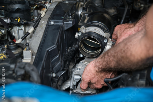 Car mechanic hands replacing engine throttle body. Mechanics workshop.