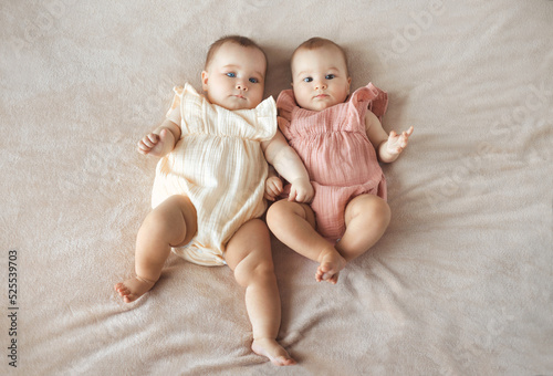 Top view of two cute baby twin girls lying together on comfortable and soft bed