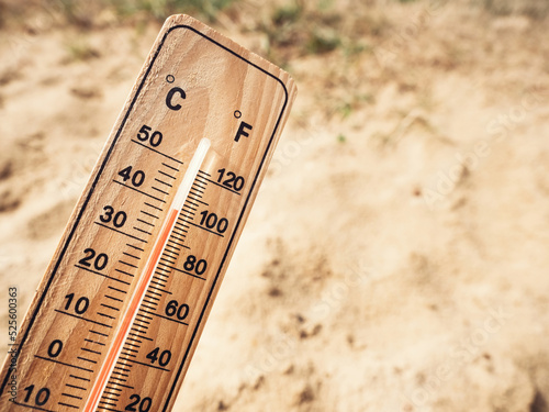 Wooden thermometer showing high temperatures over 36 degrees Celsius on sunny day on background of dry sandy ground. Concept of heat wave, warm weather, global warming, climate change.