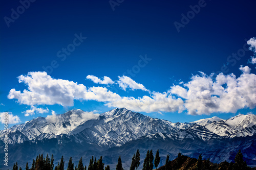 Snow covered mountains against deep blue sky and white clouds