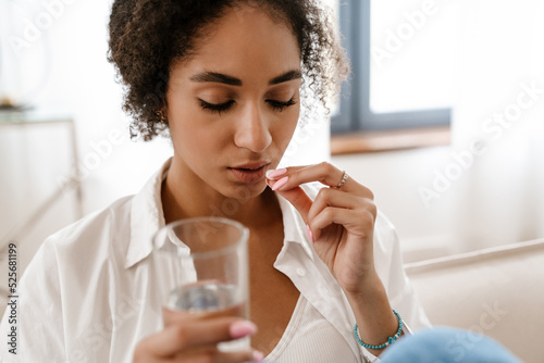 Young black woman being upset and taking abortion pill at home