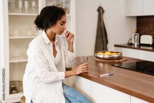 Young black woman being upset and taking abortion pill at home