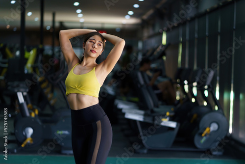 Beautiful Asian woman in sporty workout clothes showing off her perfect figure, warming up to relieve fatigue in gym workout.