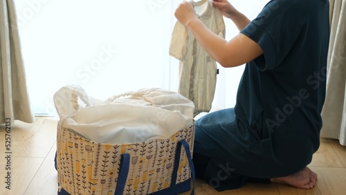 妊婦が出産のための入院準備として赤ちゃん用の服のロンパースを畳んでいる写真