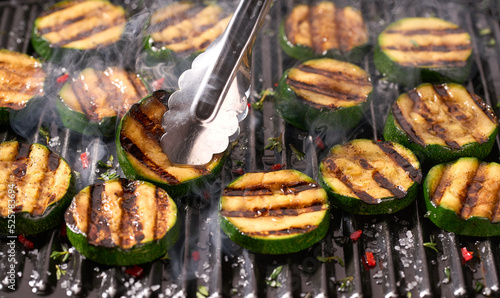 Grilling ripe zucchini on hot grid grill, selective focus. Close-up view with smoke.