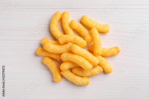 Heap of tasty cheesy corn puffs on white wooden table, flat lay