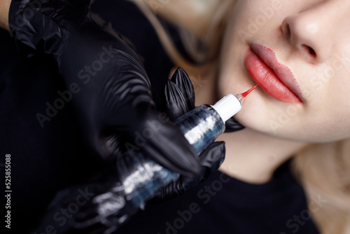 Cosmetologist master apply red permanent lips tattoo on young woman