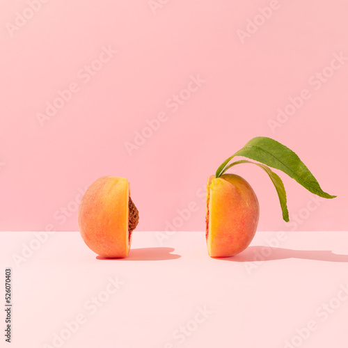 Fresh ripe organic peach with pit and leaves cut in half against bright peach pink background. Minimal fruit concept. Healthy juicy food trendy composition.