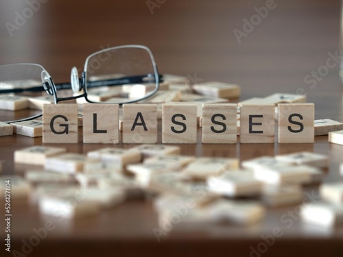 glasses word or concept represented by wooden letter tiles on a wooden table with glasses and a book