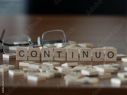 continuo palabra o concepto representado por baldosas de letras de madera sobre una mesa de madera con gafas y un libro