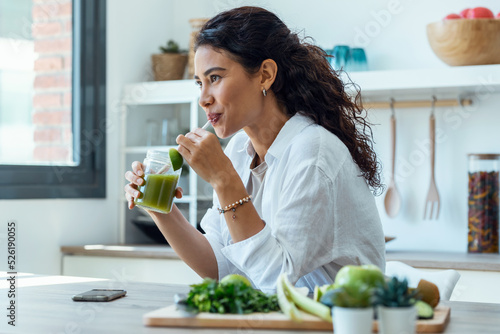 Pretty woman looking to sideways while drinking fruit detox juice in the kitchen at home.