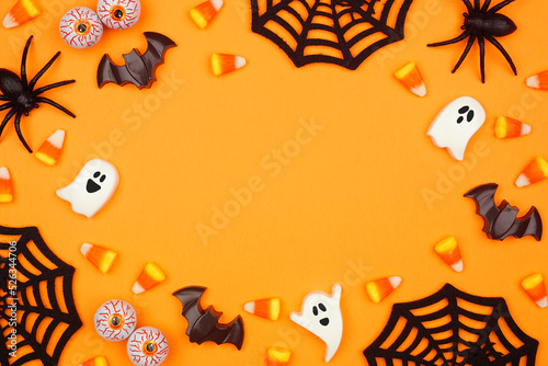 Halloween frame of scattered candy and decor. Top down view over an orange background with copy space.