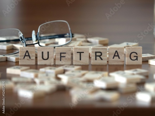 auftrag Wort oder Konzept dargestellt durch hölzerne Buchstabenfliesen auf einem Holztisch mit Brille und einem Buch