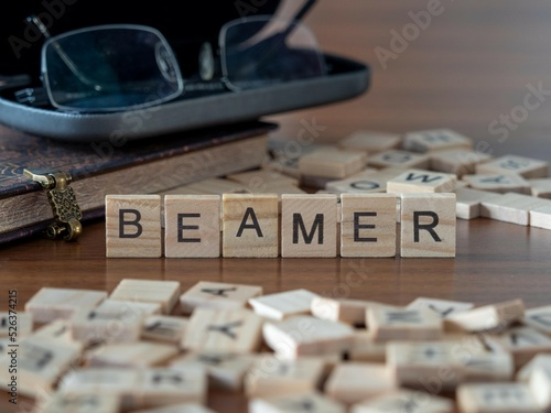 beamer Wort oder Konzept dargestellt durch hölzerne Buchstabenfliesen auf einem Holztisch mit Brille und einem Buch