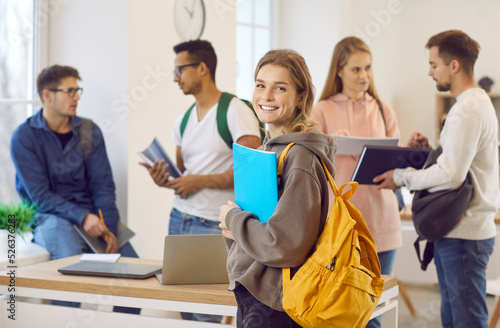 Portrait of smiling millennial Caucasian girl with backpack with groupmates in college or university. Happy young female schoolgirl satisfied with school course or training. Education concept.