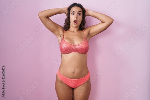 Young hispanic woman wearing lingerie over pink background crazy and scared with hands on head, afraid and surprised of shock with open mouth