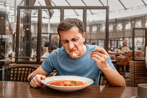 dissatisfied unhappy customer of the restaurant sniffs the disgusting smell of a bowl of soup with spoiled ingredients and is going to complain to the chef