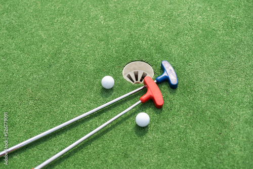 Mini-golf clubs and balls of different colors laid on artificial grass