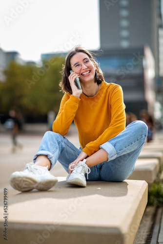 Smiling woman talking on phone sitting on bench outside in the city