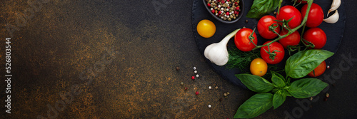 Food banner, fresh ripe red and yellow tomatoes, spices and basil leaves, garlic and green onions on dark board, healthy food concept, copy space, top view