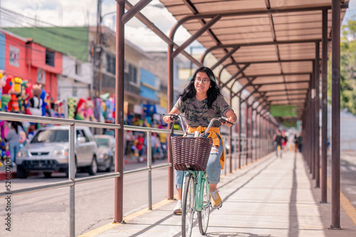 The bus station in the city. Beautiful Hispanic teen riding a bike on the street.