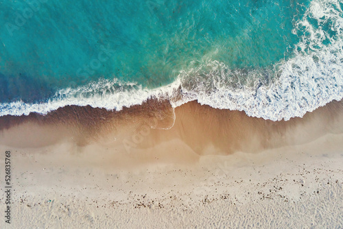 Sand beach with sea waves, top view. Summer vacation and travel concept. Beautiful coastline with blue sea and sand beach, aerial view