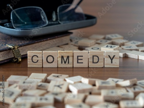 comedy word or concept represented by wooden letter tiles on a wooden table with glasses and a book