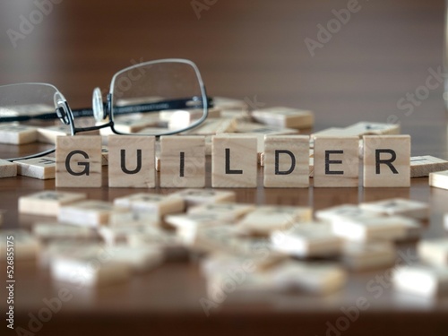 guilder word or concept represented by wooden letter tiles on a wooden table with glasses and a book