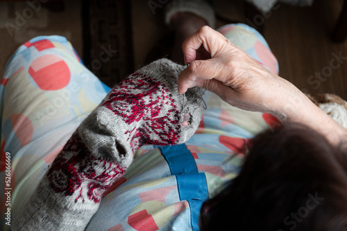 Close up of old lady hands darning winter socks with hole. Poverty in world economic crisis concept 