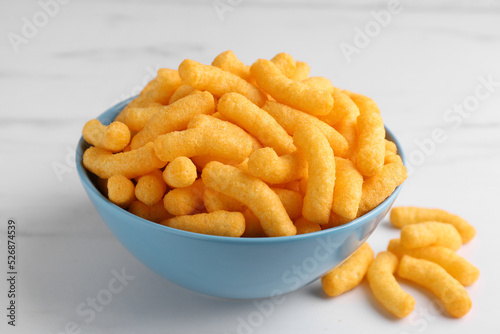 Many tasty cheesy corn puffs on white marble table