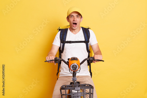 Fast transport express home delivery. Online order. Delivery man in cap with thermo backpack on electric scooter positing isolated on yellow background.