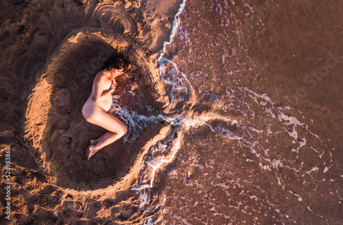 Mujer embarazada tumbada en la arena simulando un útero y el cordón umbilical. 