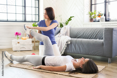Professional stretches the legs of a young woman on the floor