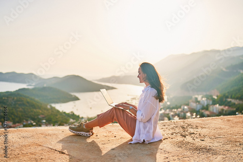Free happy inspired freelancer girl enjoys remote works at a computer at sunset with beautiful view. Online working everywhere