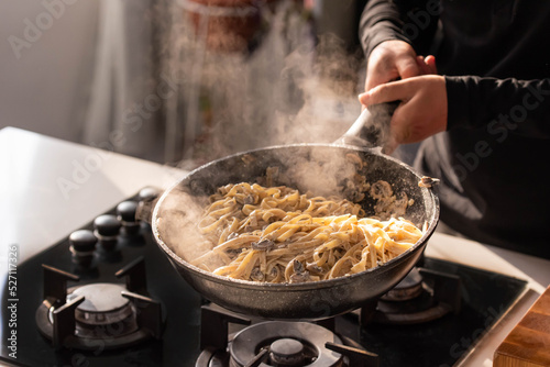 Professional chef cook making Italian Tagliatelle pasta with mushrooms and cream at kitchen gas stove in wok pan. Flying pasta levitation in motion.