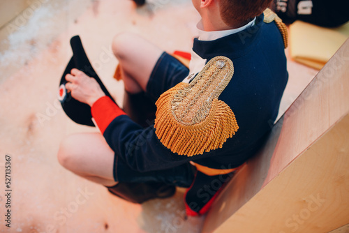 A man sits in an old vintage uniform with epaulettes in shorts.