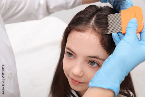 Doctor using nit comb on little girl's hair indoors. Anti lice treatment