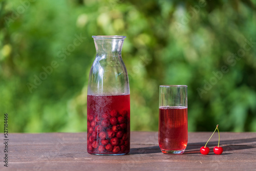 Homemade cherry brandy in a glass and in a glass bottle on a wooden table in a summer garden