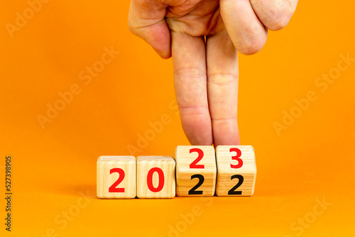 2023 happy new year symbol. Businessman turns cubes, symbolize the change from 2022 to the new year 2023. Beautiful orange table orange background. Copy space. Business 2023 happy new year concept.