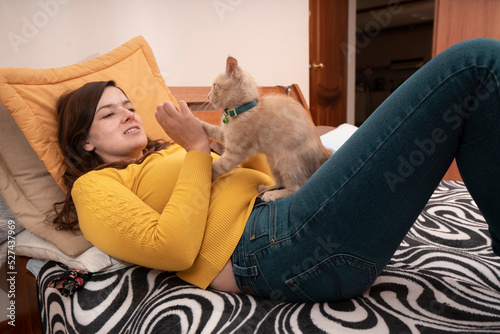 Beautiful Hispanic young woman lying on her bed playing with her little kitten with her hands