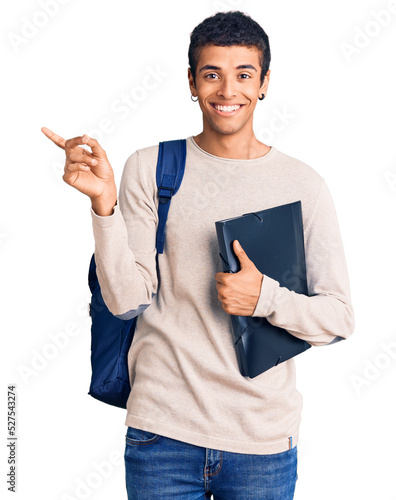 Young african amercian man wearing student backpack holding binder smiling happy pointing with hand and finger to the side
