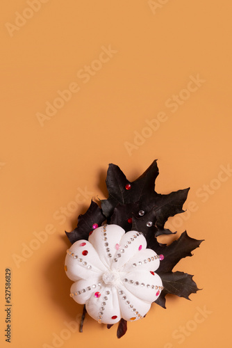 White decorative hand made pumpkin with shiny stones and maple leaves on colored background. Thanksgiving day concept.