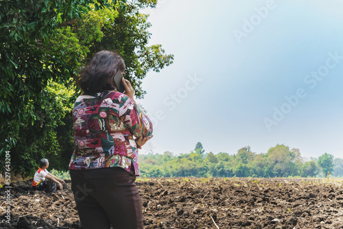 Back view of Asian elderly woman farmer use phone for business to plan farming in wilderness. Female farmers consult with landowners to cultivate crops in soil field. Farm and agricultural business.