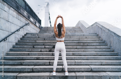 Unrecognizable female athlete warming up on stairway during workout on street