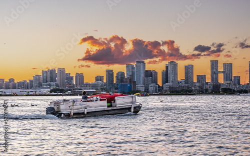 A pontoon boat loaded with colorful kayaks heads across Toronto's Inner Harbour with the city skyline, and airport and the sunset in the background.