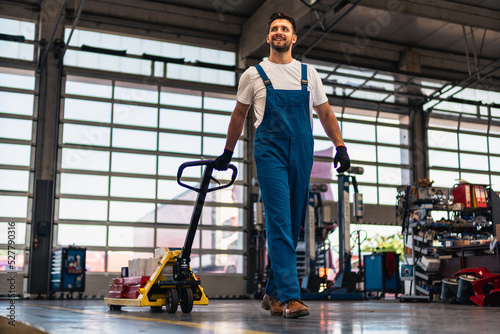 Caucasian professional male mechanic pulls, trolley with repair parts. Service, maintenance, people concept. Side view. Selective focus. Web Banner