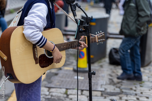 Busker. Singer guitarist street musician with acoustic guitar. Close up with selective focus on foreground.