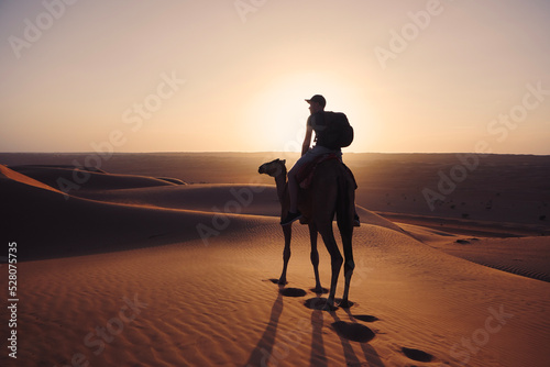 Camel riding in desert at golden sunset. Man enjoying journey on sand dunes. Wahiba Sands in Sultanate of Oman..
